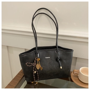 Detail of black matte leather tote bag with Fashion lettering and golden metal charms