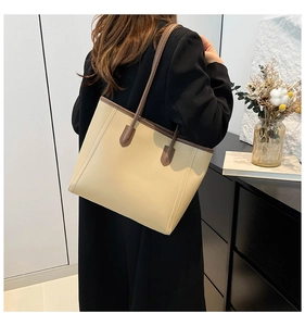 Side view of a large cream tote bag with brown handles being worn by a female model