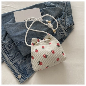 Detailed shot of a white corduroy bucket bag with red strawberry prints and drawstring cord