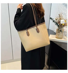 Detail of minimalist beige leather tote bag with dark brown handles shown on shoulder