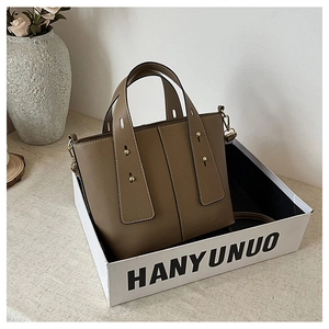 Brown leather bucket bag with wide handle and gold rivets inside a branded gift box