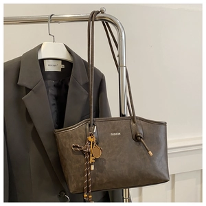 Detail of dark brown leather tote bag with FASHION text and vintage charms on hanger