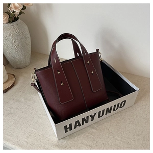 Detail of burgundy bucket bag with white stitching and golden metal hardware hooks