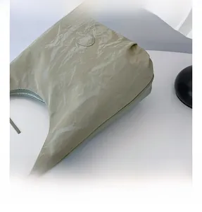 Detail showing the pleated texture and oval leather tag on a light green tote bag