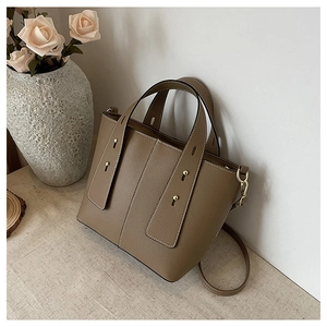 Close-up of brown pebbled leather bucket bag with white contrast stitching and gold rivets
