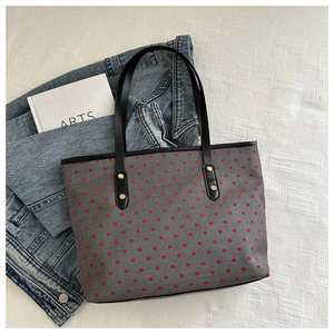 Macro detail of gray tote bag with red heart embroidery, black handles and gold rivets