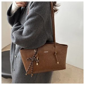 Brown vintage tote bag detail showing knotted handle and fashion print on leather surface