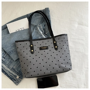 Detail of grey canvas tote bag with black dots and leather straps on linen background