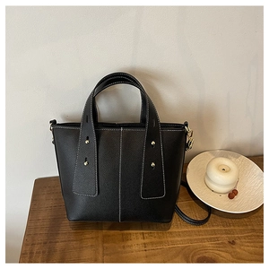 Detail of black leather tote bag with white contrast stitching and gold metal studs