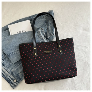 Flat lay of black tote bag with red heart prints and gold metal logo plate detail