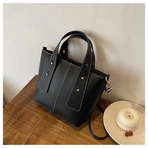 Detail of black lychee grain leather tote bag with white stitching and gold hardware