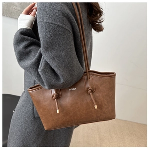 Close-up of brown textured leather tote bag with fashion logo and knotted handle detail