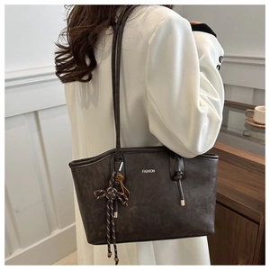 Detail of a large brown leather tote bag with fashion lettering and metallic charms