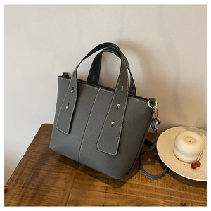 Close-up of a dark grey tote bag with white contrast stitching and gold metal rivets
