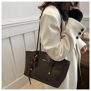 Detail of dark brown tote bag with FASHION text and woven rope charm on white coat