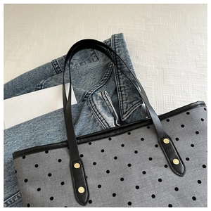 Detail of grey star-print tote bag featuring black slim handles and metallic gold rivets