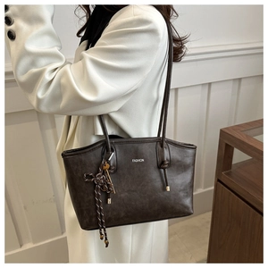Detail of a dark brown tote bag featuring white FASHION print and woven rope charm