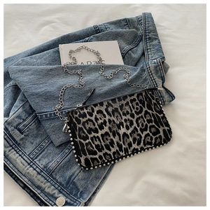 Flat lay of leopard print shoulder bag with silver studs and chain on denim jacket