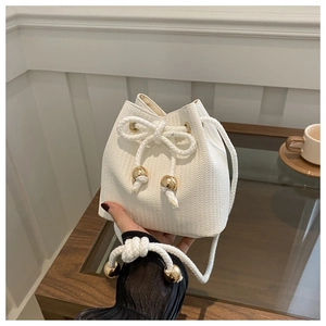 Detail of white woven bucket bag featuring rope drawstring and gold metal sphere charms