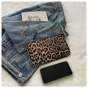 Detail of leopard print crossbody bag with silver studs on blue denim jacket