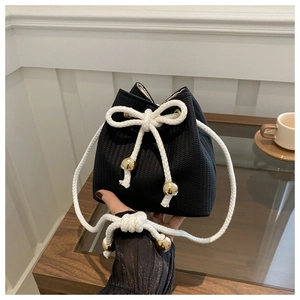 Detail view of woven black bucket bag with white drawstring and gold metal sphere stoppers