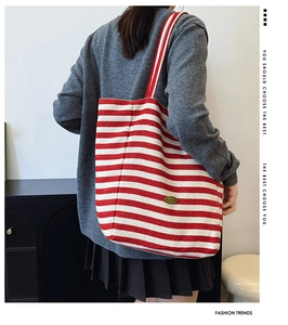 Detail of red and white striped canvas tote bag with gold logo on a shoulder strap