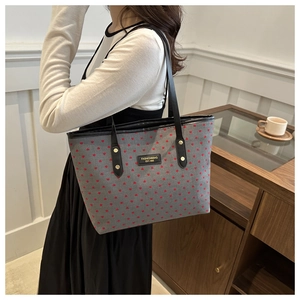 Detailed view of grey tote bag with red heart pattern and metal logo on a model