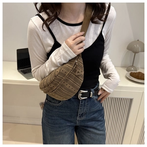 Detail of brown woven crossbody bag with knit texture and wide fabric strap on a desk