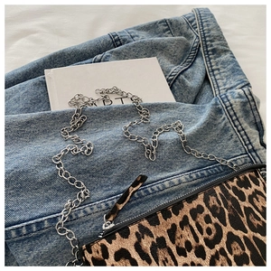 Close-up of leopard print crossbody bag with silver chain strap on denim fabric