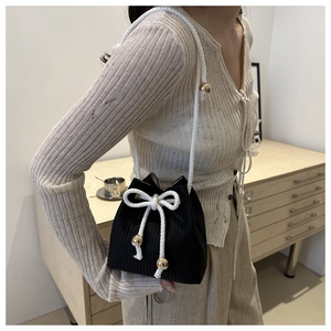 Detail of black knit bucket bag featuring white rope drawstring and gold metal ball charms