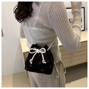 Detail of black corduroy bucket bag with strawberry embroidery and bow drawstring