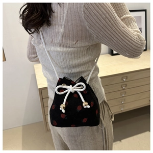 Detail of black corduroy bucket bag featuring red strawberry embroidery and white drawstrings