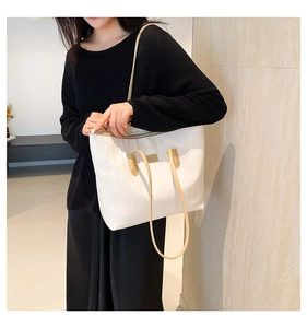 Close-up of cream and khaki tote bag with metal nameplate on a model's shoulder