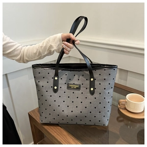 Close-up of stylish gray polka dot tote bag with black leather straps and fashion label