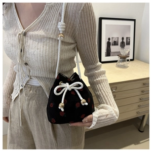 Detail of black corduroy bucket bag with strawberry embroidery and white rope strap