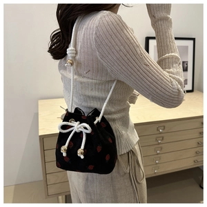 Detail of black strawberry bucket bag with white drawstring and gold metal accents