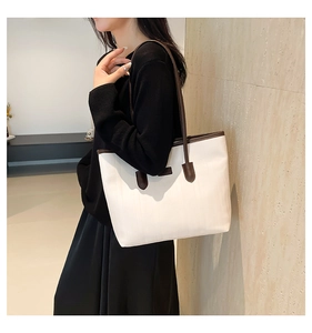 Detail of a large beige tote bag with brown leather handles worn over the shoulder