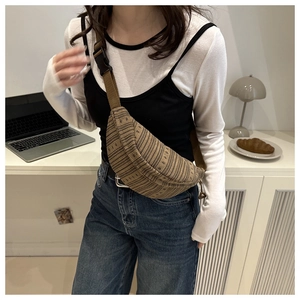 Detail of a brown woven textured crossbody chest bag with adjustable strap worn by a model