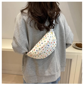Close-up of a white canvas chest bag with colorful polka dots on a female model