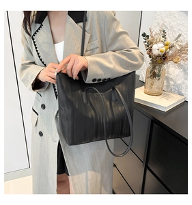 Detail of black tote bag featuring vertical pleated texture and elegant metal brand plate