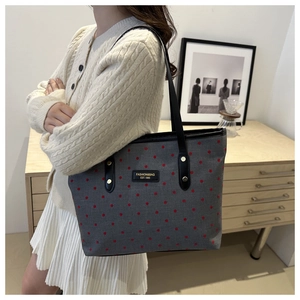 Detailed shot of grey tote bag with red polka dots and black leather handles on a table