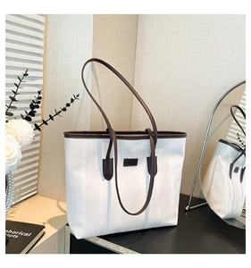 Detail of white canvas tote bag with brown leather handles and logo patch on wooden surface