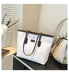 Detail of white striped tote bag with brown leather handles and brand logo patch