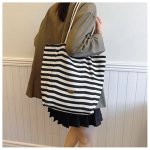 Detail showing high-capacity black and white striped canvas tote bag worn on shoulder