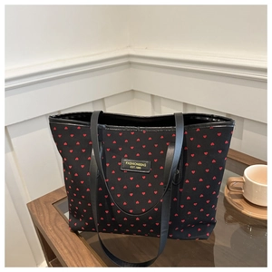 Detail of black canvas tote bag with red heart print and brand logo on a coffee table