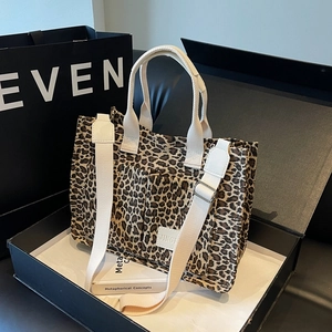 Large leopard print tote bag with wide straps and branding in a luxury display setting