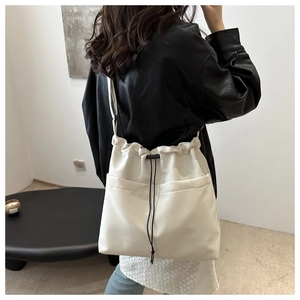Detail of off-white drawstring crossbody bag featuring dual front pockets and black closure