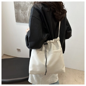 Detailed view of a white leather drawstring bucket bag worn over a black leather jacket