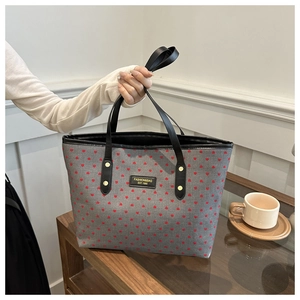 Detail of grey tote bag with red heart pattern, black handles and gold rivet accents