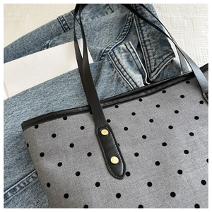 Close-up of grey polka dot tote bag featuring black leather straps and gold metal rivets